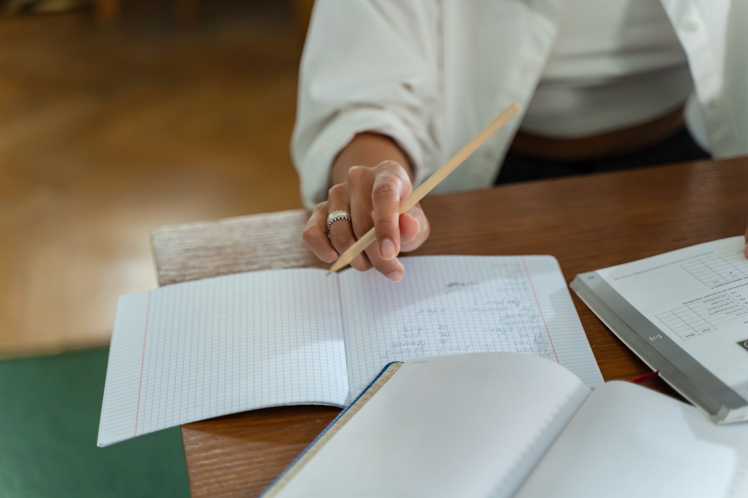 Close-up of a person writing in a graph notebook with a pencil at a wooden table, ideal for study and education themes.